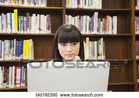 Stock Image - Asian woman using laptop in library. Fotosearch