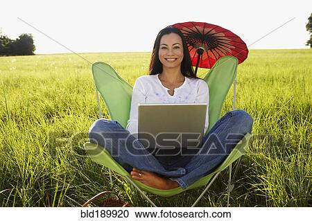 Stock Image - Asian woman using laptop in meadow. Fotosearch