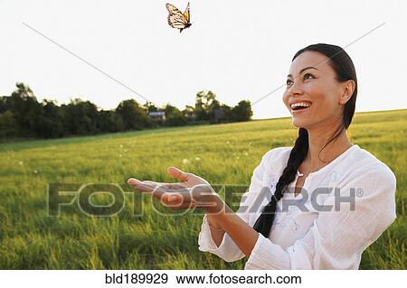 Stock Photo - Asian woman watching butterfly in meadow. Fotosearch