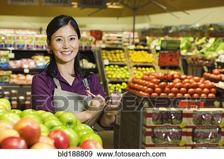 Asian woman working in produce section of grocery store View Large Photo Image Stock Photo - Asian woman working in produce section of grocery store. Fotosearch