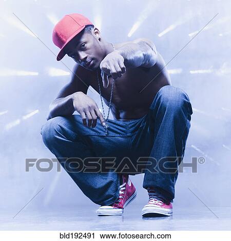 Stock Image - Back lit African man squatting and pointing. Fotosearch