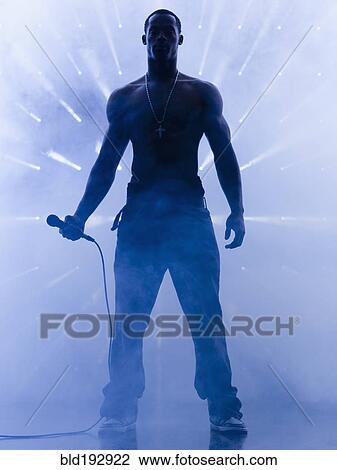 Stock Image - Back lit African singer holding microphone. Fotosearch
