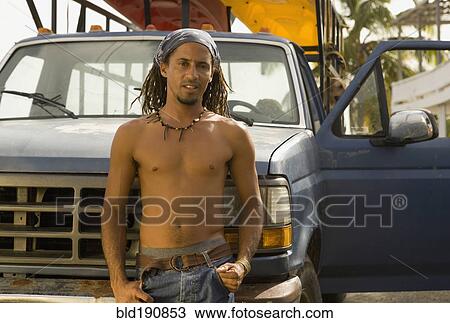 Stock Image - Bare chested Hispanic man leaning against front of truck. Fotosearch
