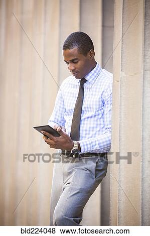 Stock Photo - Black businessman leaning on wall using digital tablet. Fotosearch