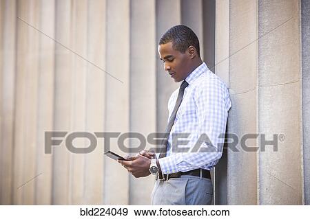 Black businessman leaning on wall using digital tablet View Large Photo Image Stock Photo - Black businessman leaning on wall using digital tablet. Fotosearch