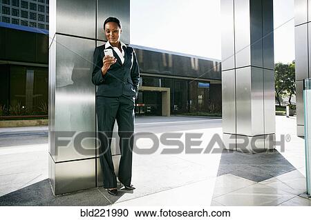 Stock Image - Black businesswoman using cell phone outdoors. Fotosearch