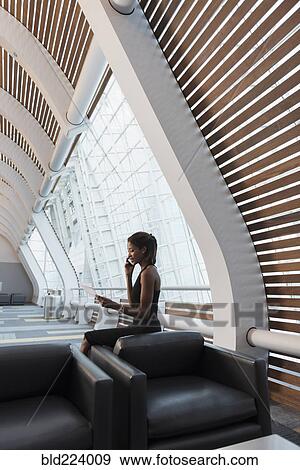 Stock Photo - Black businesswomen reading paperwork using cell phone. Fotosearch