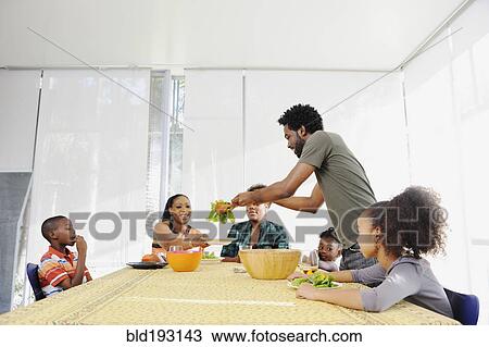 Stock Image - Black family eating salad at dining room table. Fotosearch