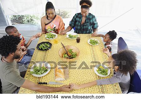 Picture - Black family saying grace at dining room table. Fotosearch
