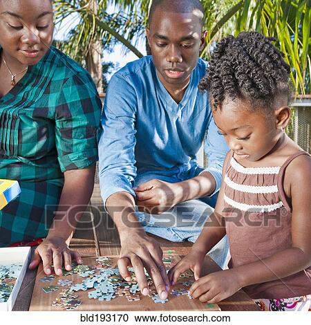 Stock Image - Black father and mother solving puzzle with child. Fotosearch