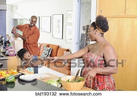 Stock Image - Black girl helping mother prepare food in kitchen. Fotosearch