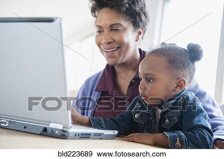 Stock Photo - Black grandmother and granddaughter using laptop. Fotosearch
