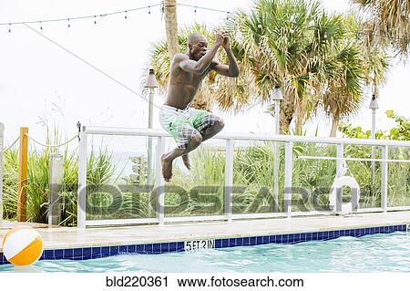 Stock Image - Black man jumping into swimming pool. Fotosearch