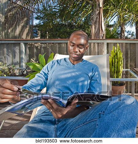 Stock Image - Black man reading book on patio. Fotosearch