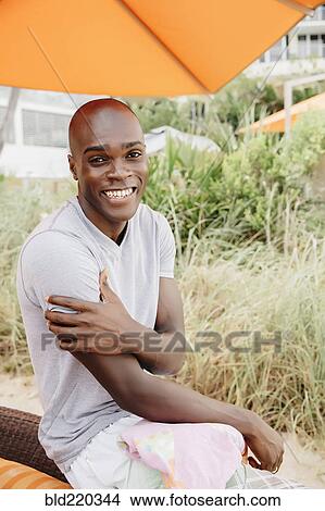 Black man sitting under umbrella on beach View Large Photo Image Picture - Black man sitting under umbrella on beach. Fotosearch