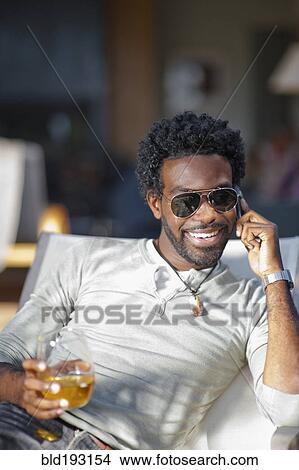 Picture - Black man talking on cell phone and drinking. Fotosearch