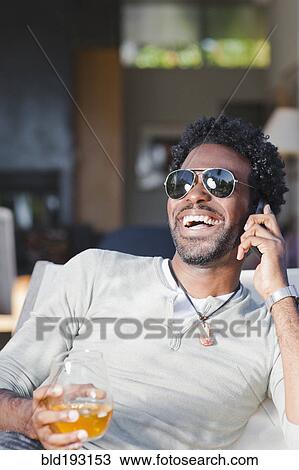 Stock Image - Black man talking on cell phone and drinking. Fotosearch