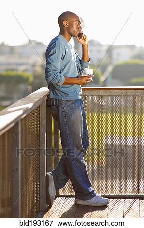 Stock Photo - Black man talking on cell phone on balcony. Fotosearch
