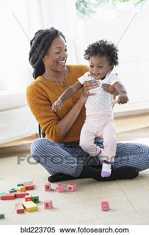 Stock Photography - Black mother and baby daughter playing with blocks on carpet. Fotosearch