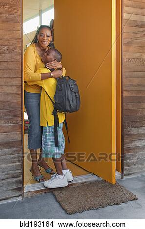 Picture - Black mother greeting son at front door. Fotosearch