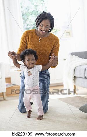 Stock Photo - Black mother helping baby daughter learn walking. Fotosearch