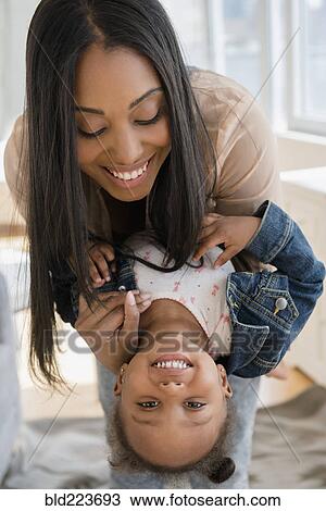 Stock Image - Black mother holding baby daughter upside-down. Fotosearch