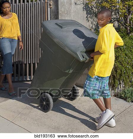 Stock Image - Black mother watching son wheel garbage can. Fotosearch