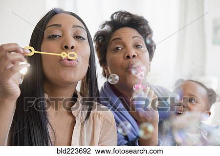 Stock Image - Black multi-generation family blowing bubbles with bubble wand. Fotosearch