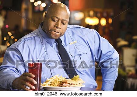 Stock Photograph - Black police officer eating unhealthy food. Fotosearch