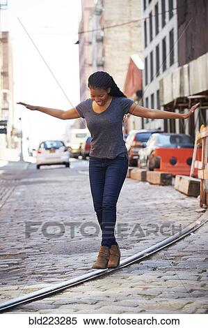 Stock Photography - Black woman balancing on track in cobblestone city street. Fotosearch