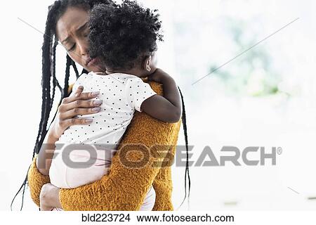 Picture - Black woman holding and comforting baby daughter. Fotosearch
