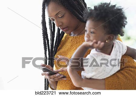 Black woman holding baby daughter using cell phone View Large Photo Image Stock Image - Black woman holding baby daughter using cell phone. Fotosearch
