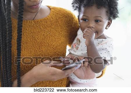 Black woman holding baby daughter using cell phone View Large Photo Image Stock Image - Black woman holding baby daughter using cell phone. Fotosearch