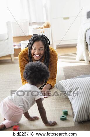Stock Photo - Black woman playing with baby daughter on carpet. Fotosearch