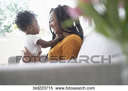Stock Photography - Black woman playing with baby daughter on sofa. Fotosearch