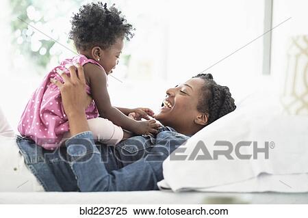 Stock Photography - Black woman playing with baby daughter on bed. Fotosearch