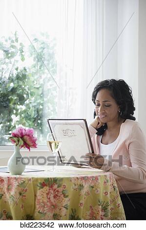 Stock Image - Black woman reading menu in restaurant. Fotosearch
