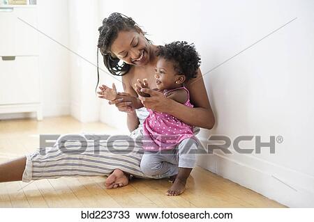 Black woman sitting on floor kissing clapping hands with baby daughter View Large Photo Image Stock Image - Black woman sitting on floor kissing clapping hands with baby daughter. Fotosearch