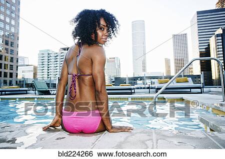 Stock Photograph - Black woman sitting poolside looking over shoulder. Fotosearch