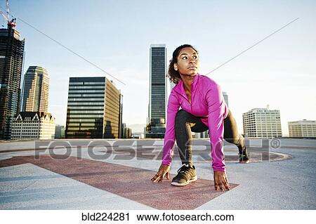 Stock Image - Black woman stretching legs on urban rooftop. Fotosearch