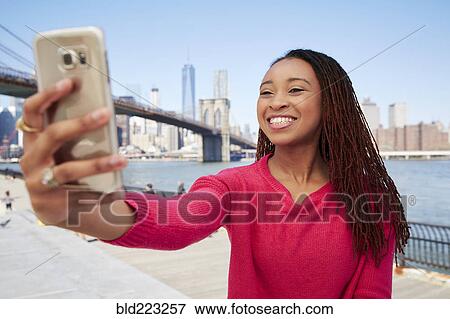 Stock Photo - Black woman taking selfie at waterfront. Fotosearch