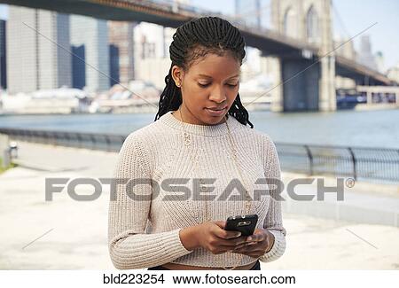 Picture - Black woman using cell phone at waterfront. Fotosearch