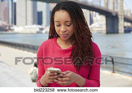 Stock Photo - Black woman using cell phone at waterfront. Fotosearch
