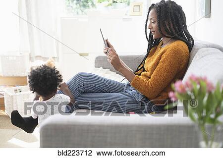 Black woman using digital tablet on sofa near baby daughter View Large Photo Image Stock Image - Black woman using digital tablet on sofa near baby daughter. Fotosearch