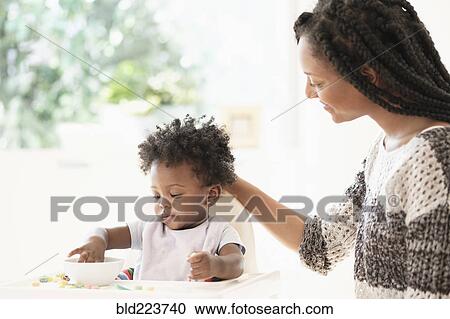 Black woman watching baby daughter eat cereal in high chair View Large Photo Image Stock Image - Black woman watching baby daughter eat cereal in high chair. Fotosearch