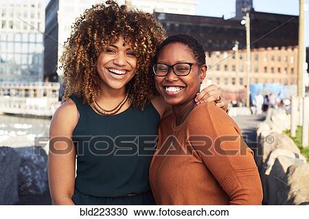 Stock Image - Black women hugging and smiling at waterfront. Fotosearch