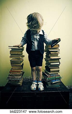 Stock Photo - Boy holding cell phone near stacks of books. Fotosearch