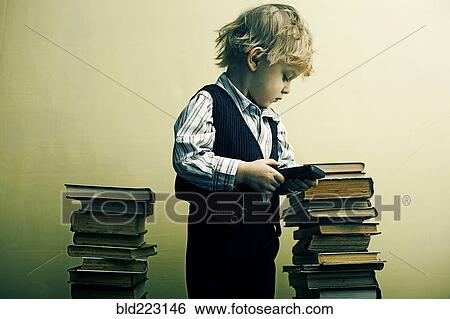 Stock Photograph - Boy holding cell phone near stacks of books. Fotosearch