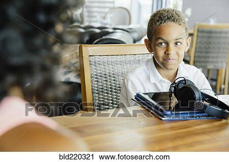 Stock Image - Boy with digital tablet sitting at restaurant. Fotosearch