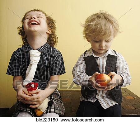 Stock Image - Brother and sister laughing and holding apple on table. Fotosearch